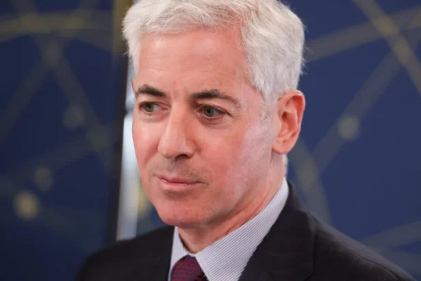 Portrait of a middle-aged man with silver hair in a dark suit, looking to the right against a blue abstract background.