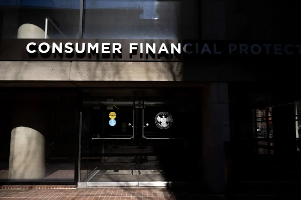 Front entrance of a government building with a large 'CONSUMER FINANCIAL PROTECTION' sign above glass doors and a visible federal seal on the door.