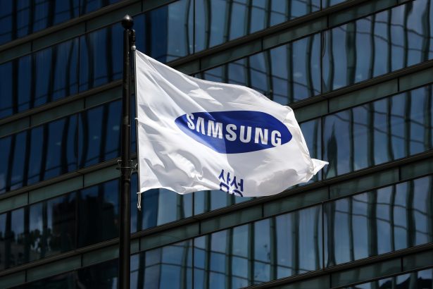 White Samsung flag fluttering on a flagpole in front of a glass office building with blue-tinted windows