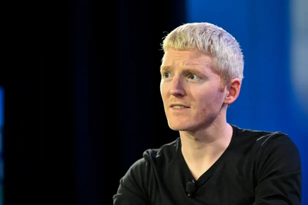 Blond man in a black shirt with a clip-on mic on stage, looking to the left.