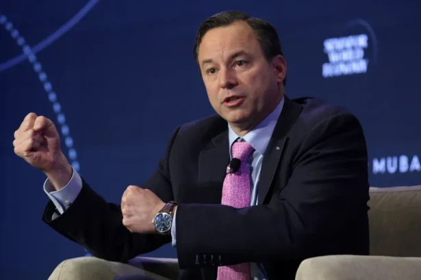Man in a dark suit and pink tie gesturing with fists while speaking on a panel stage