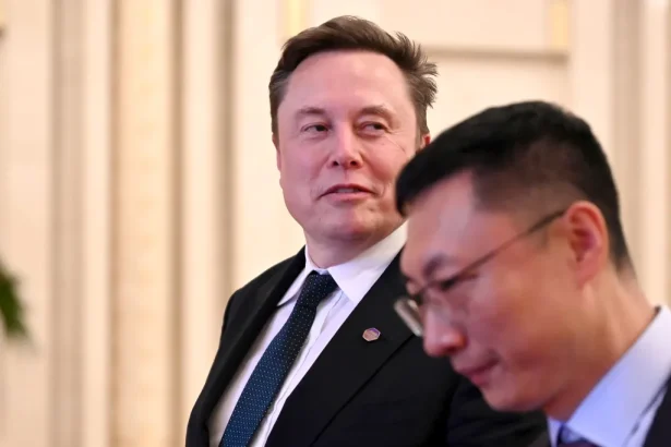 Two men in suits in a bright indoor setting; one looks toward the other as they converse.