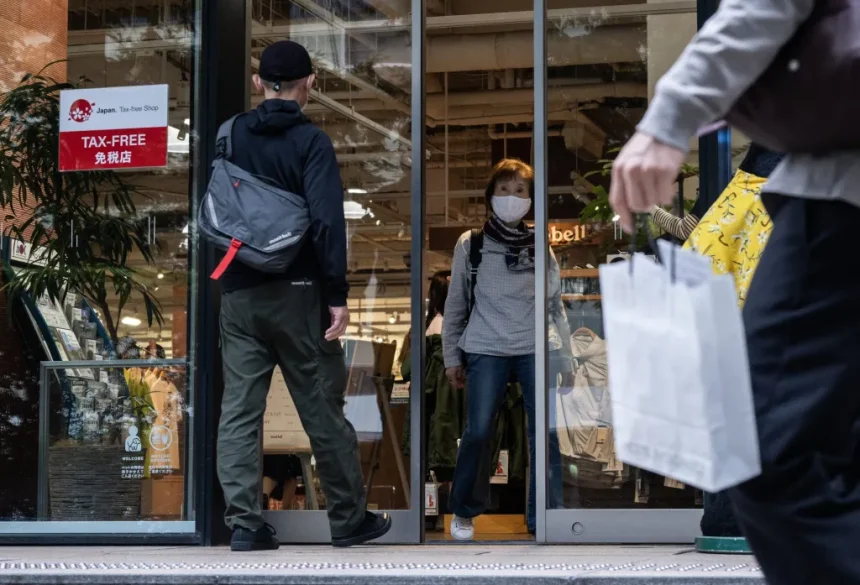Shoppers enter a storefront through glass doors; a masked woman stands inside as a man with a backpack approaches the entrance.