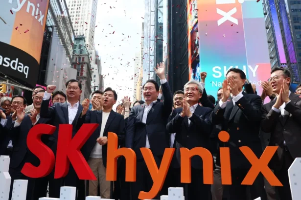 Businesspeople in suits celebrate in Times Square behind large red SK hynix letters with confetti in the air.