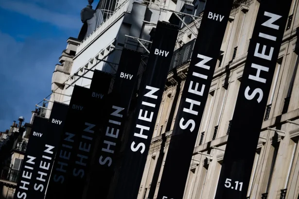 Tall black banners along a building spelling SHEIN with BHV logos and 5.11 at the bottom, against a blue sky.