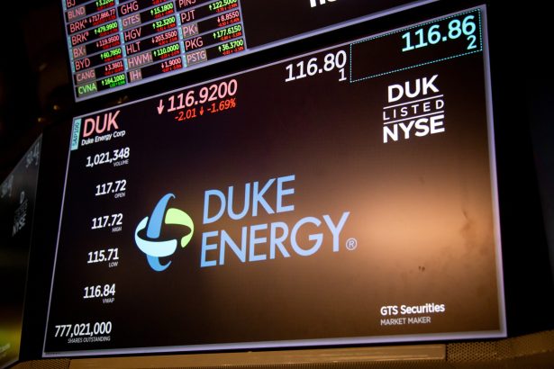 Stock ticker board showing Duke Energy (DUK) with NYSE logo and Duke Energy name, price 116.80 displayed prominently, market data in the background