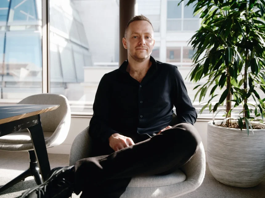 Nscale CEO Josh Payne sitting in an office chair near a window